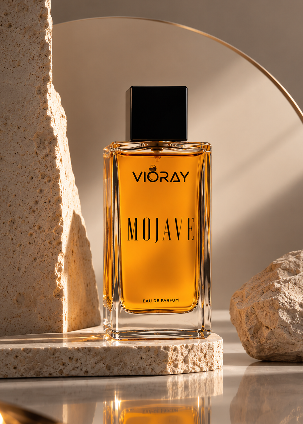 A bottle of Vioray Mojave Eau de Parfum with amber liquid and a black cap, styled on a stone platform with textured rocks and a gold arch in a warm, minimalist setting.